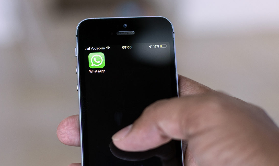Hand holding a mobile phone with the Whatsapp app and logo displayed